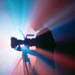 A person filming with a camera on a tripod lit in blue and red light